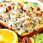 A slice of bread topped with orange cashew chicken salad with pecans and fresh oranges and lettuce.