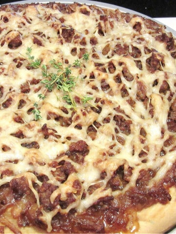A French Onion Pizza on a pizza pan with melted cheese and fresh thyme leaves.