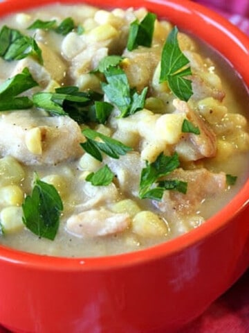 A red mug filled with Chicken Corn Chowder with Bacon and a parsley garnish.