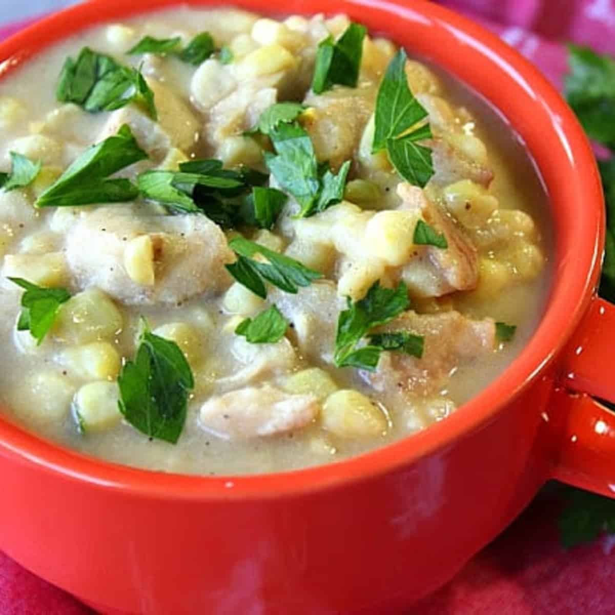 A red mug filled with Chicken Corn Chowder with Bacon and a parsley garnish.