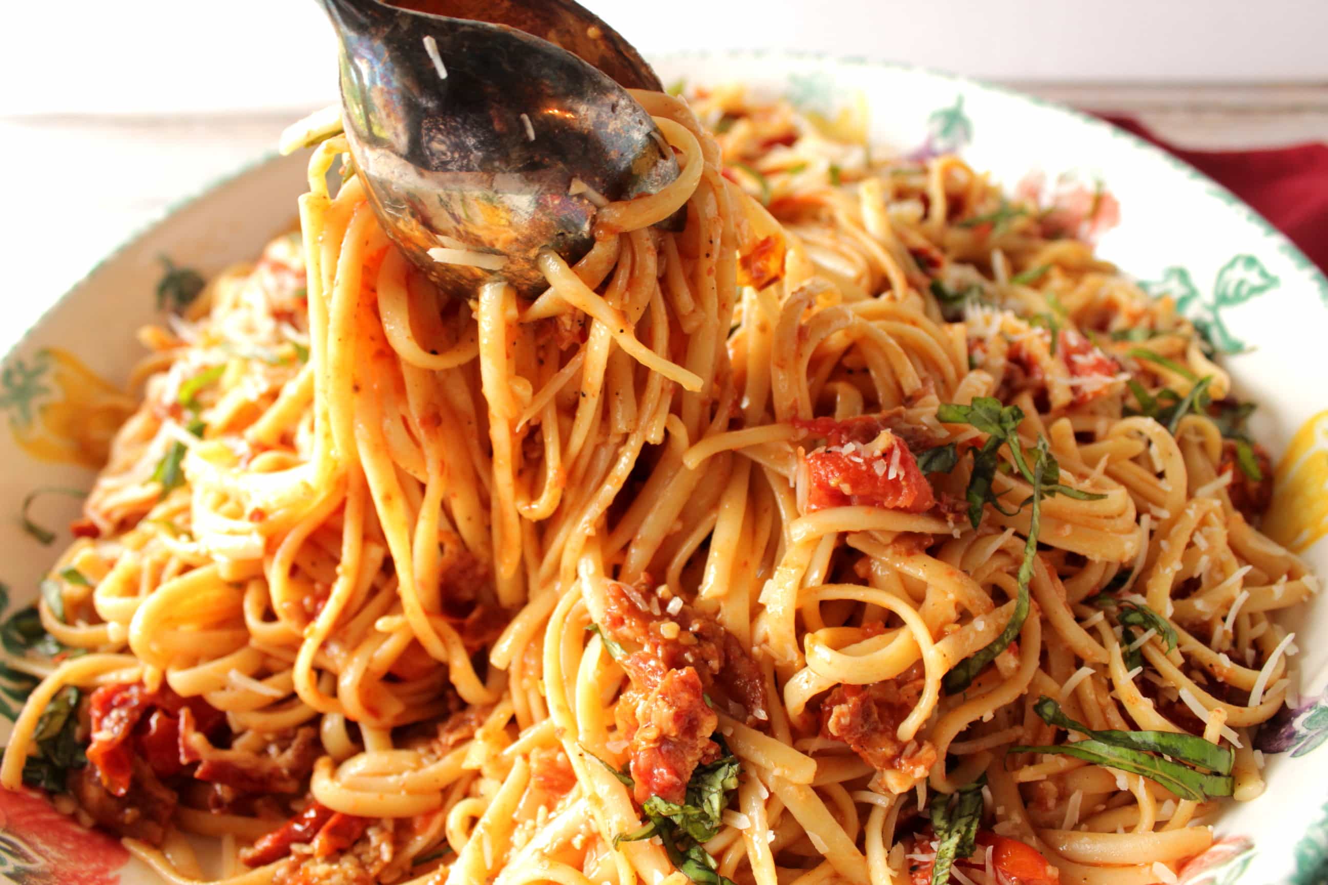 A set of tongs lifting out some linguine from a large bowl.