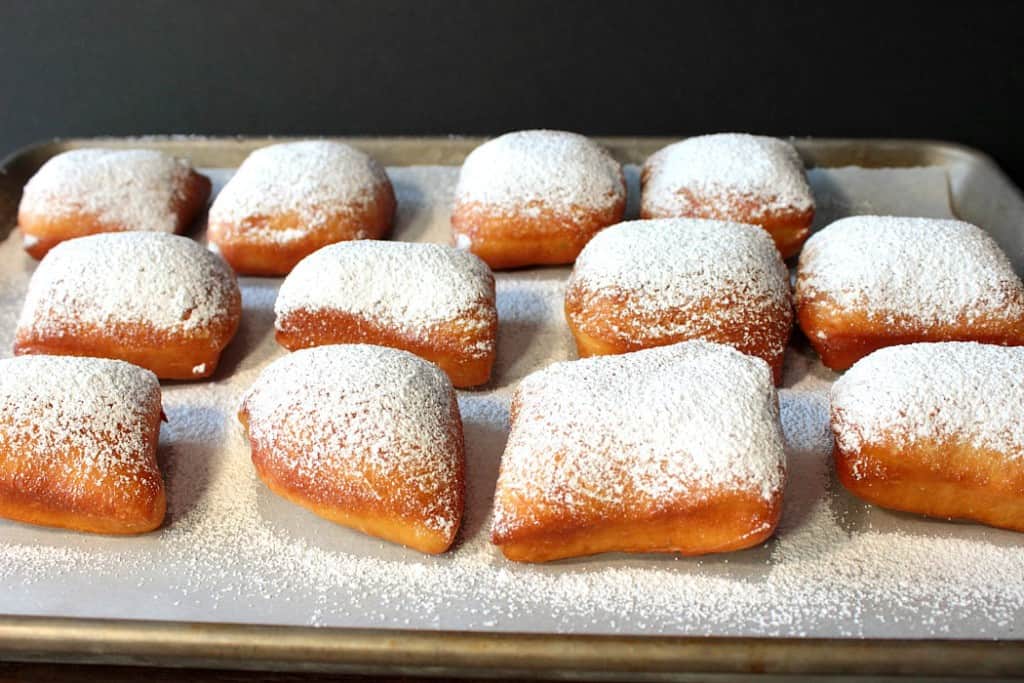 A horizontal photo of a bunch of powdered sugar beignets on a baking sheet.