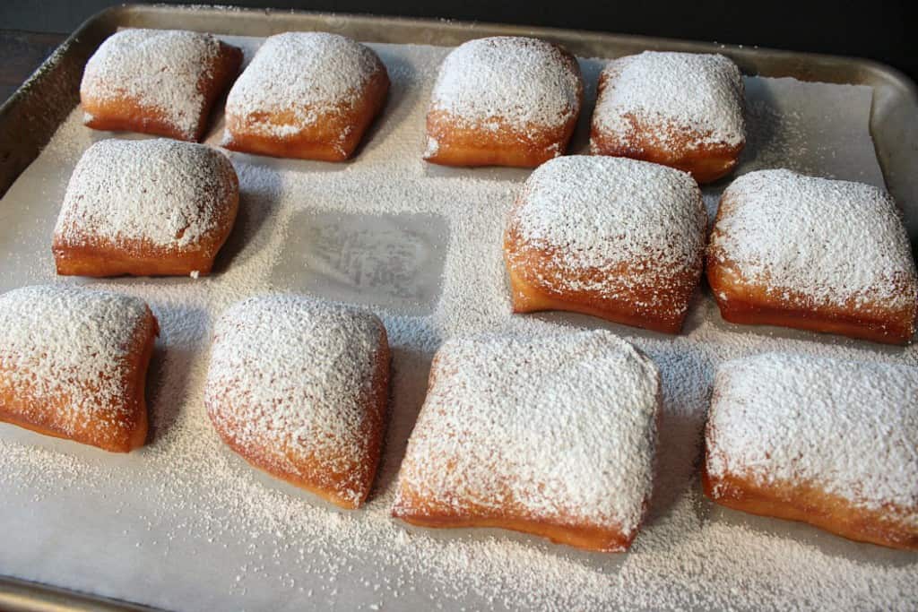 Confectioners sugar dusted homemade fried beignets on a baking sheet with parchment paper.
