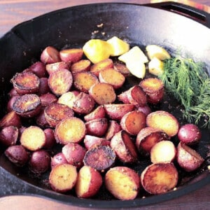 A cast iron skillet filled with Braised Red Potatoes, fresh dill and lemon.