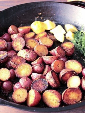 A cast iron skillet filled with Braised Red Potatoes, fresh dill and lemon.