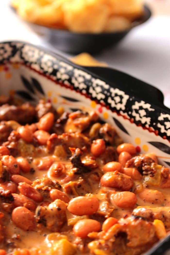 Spicy, hearty, cheesy and delicious. This Sloppy Sausage Bean Dip covers all the bases and will score you some serious points at your next party or tailgate. - Kudos Kitchen by Renee - www.kudoskitchenbyrenee.com A closeup vertical photo of Cheesy Sausage Bean Dip in a black and white casserole dish.