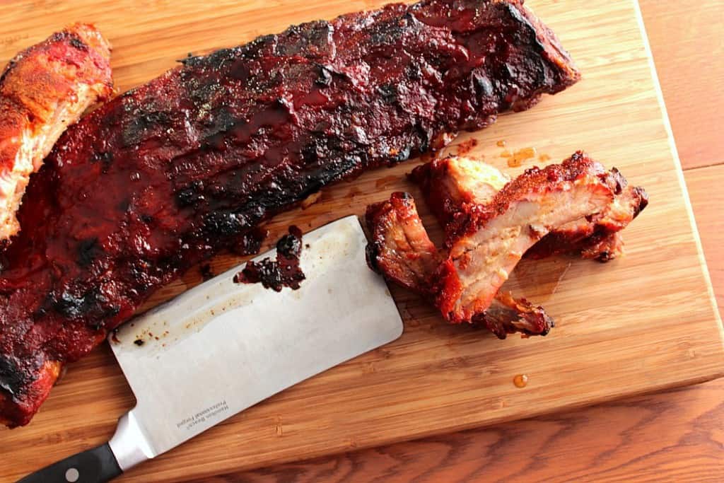 Overhead photo of a slab of baby back ribs on a wooden cutting board with a cleaver.