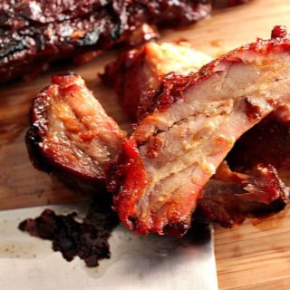 closeup photo of baby back ribs on a wooden cutting board with bbq sauce and a cleaver