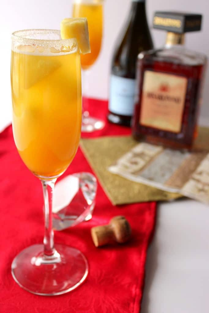 Closeup photo of a golden statue cocktail in a champagne flute with a chunk of pineapple on the rim.