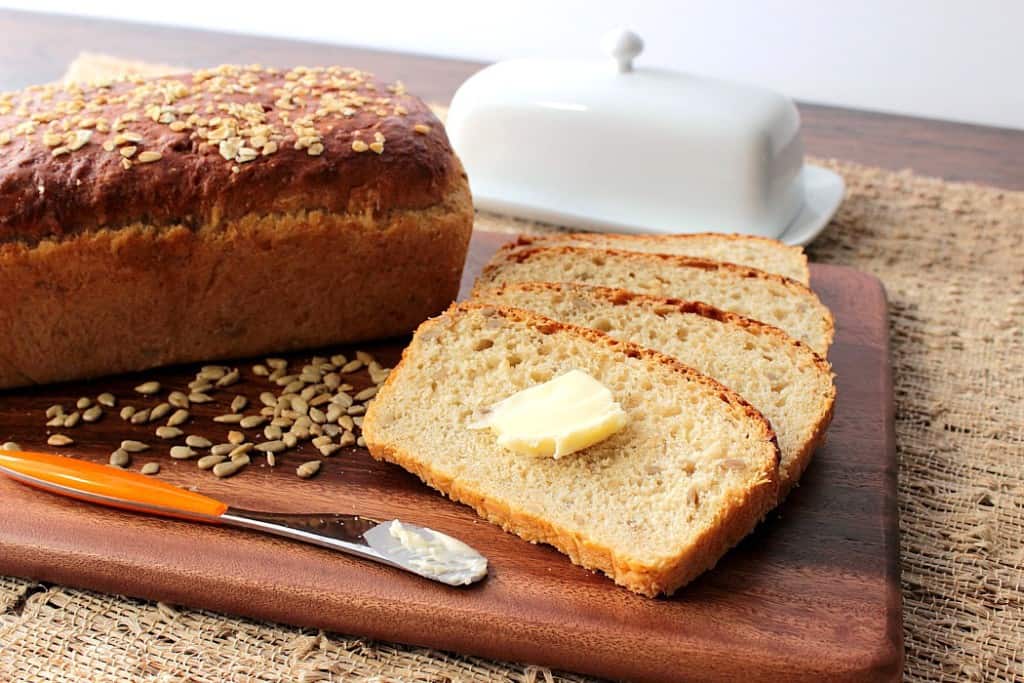 A sliced loaf of oatmeal honey bread with a pat of butter on a wooden board.