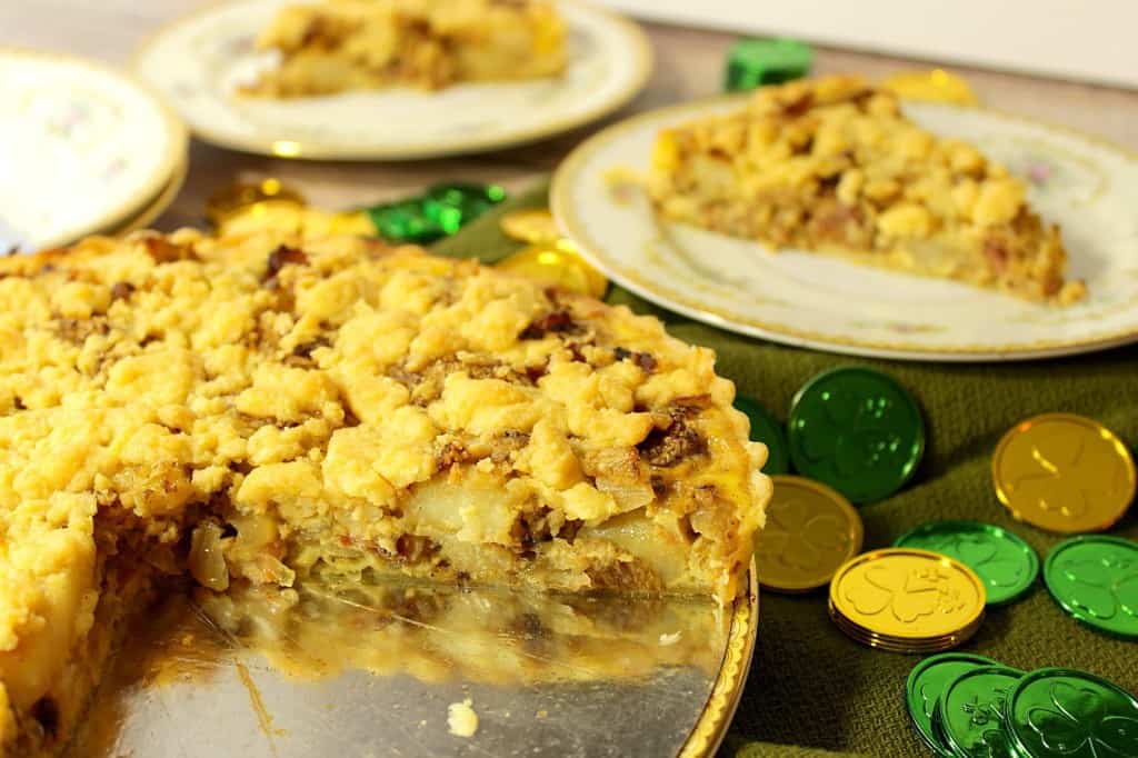 An Irish Cheese and Potato Tart with a few slices taken out and a few gold and green coins on the table.