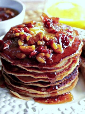 A stack of Banana Bourbon Pancakes with Walnut Bacon Maple Syrup on top.