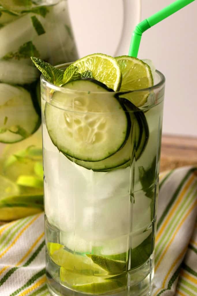 A vertical closeup photo of cucumber lime fitness water in a glass with ice and mint.