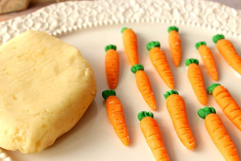 Block of homemade marzipan candy on a white plate with homemade marzipan carrots.