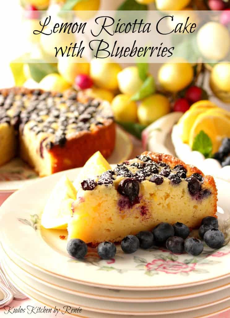 A beautiful slice of lemon ricotta cake on a pretty plate with fresh blueberries.