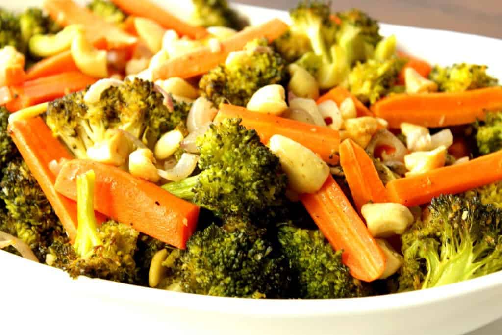 Closeup photo of chopped broccoli, carrots, and cashews in a white bowl.