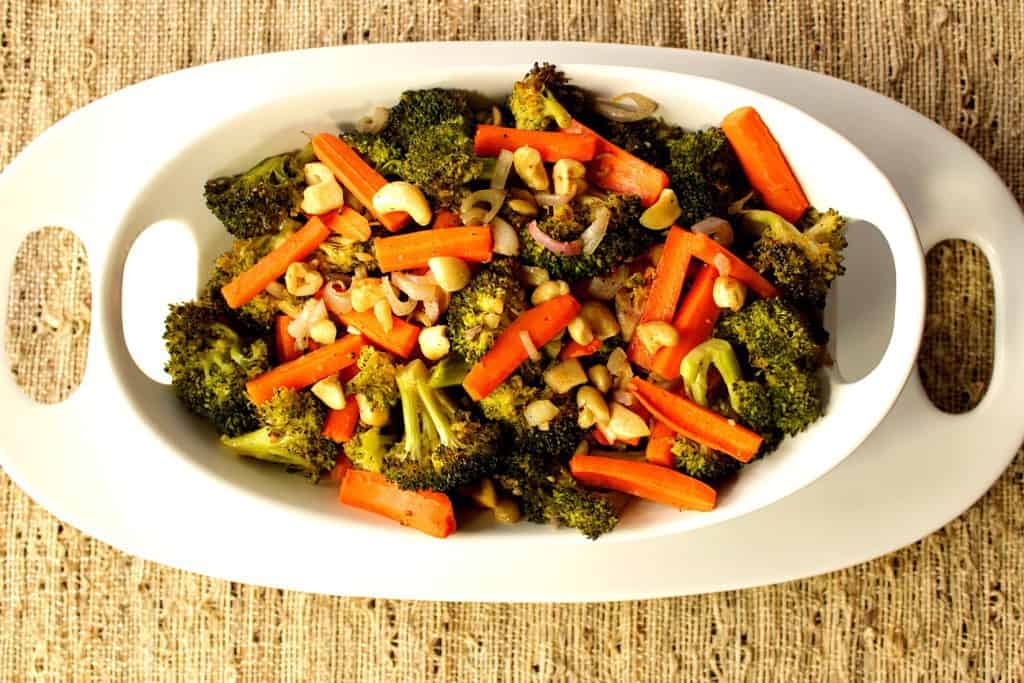 Overhead photo of carrots and broccoli in a white bowl on a white platter on a tan colored tablecloth.