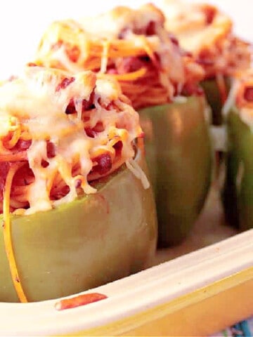 A casserole dish filled with Spaghetti Stuffed Bell Peppers topped with cheese.