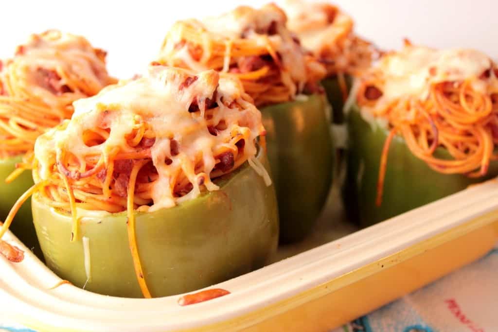 Spaghetti Stuffed Bell Peppers topped with cheese in a casserole dish.