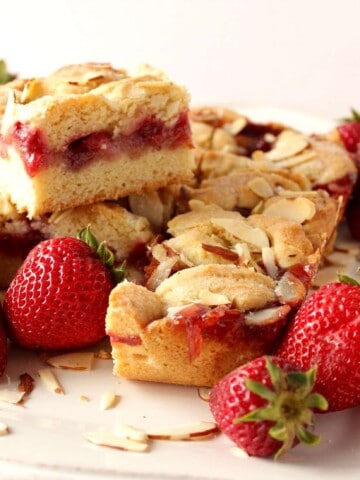 A bunch of strawberry cobbler bars on a white scalloped plate with fresh strawberries as garnish.