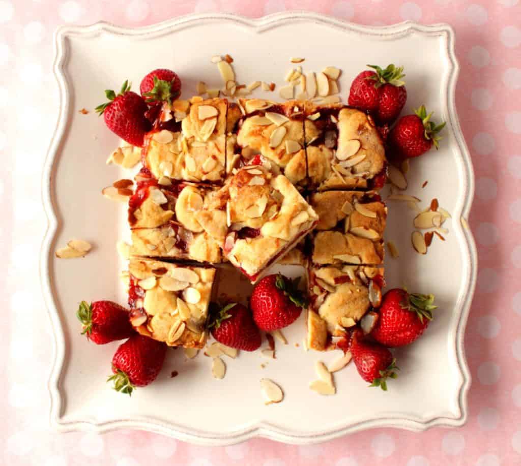 Overhead photo of a square scalloped plate filled with strawberry cobbler bars topped with almonds.