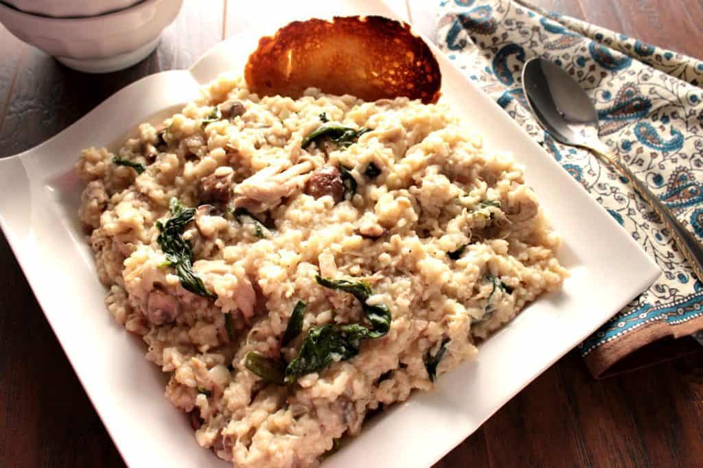 Risotto with spinach and chicken on a white square plate and a toasted piece of bread.