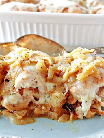 A pretty blue plate filled with French Onion Chicken Thighs with melted cheese and serving spoons.