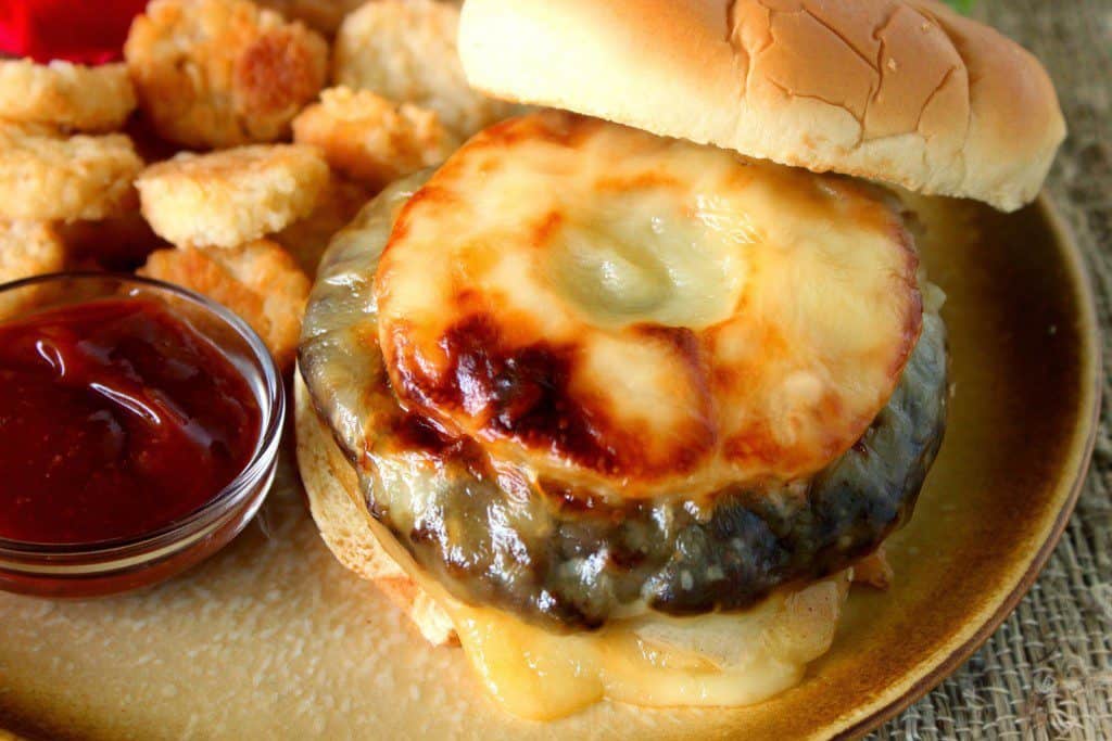 Turkey Burger with Pineapple and Swiss Cheese  on a tan plate with tater tots and sauce.