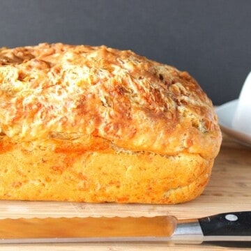 A golden brown loaf of cheesy Jalapeno Quick Bread with a serrated knife.