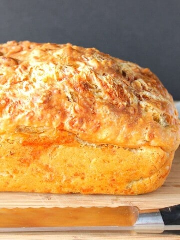 A golden brown loaf of cheesy Jalapeno Quick Bread with a serrated knife.