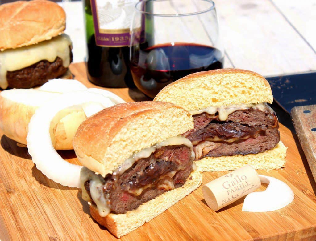 Man Burgers Stuffed with Caramelized Onions and Pinot Noir in the sunshine with a wine bottle and a glass of wine in the background.