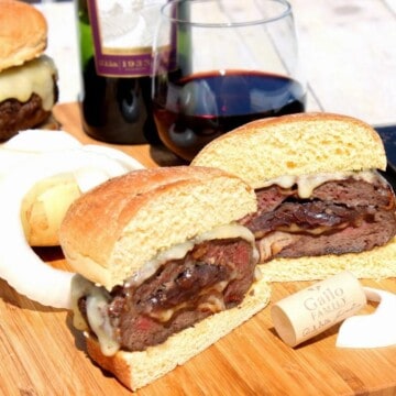 Burgers Stuffed with Caramelized Onions on a cutting board with a glass of red wine in the background.