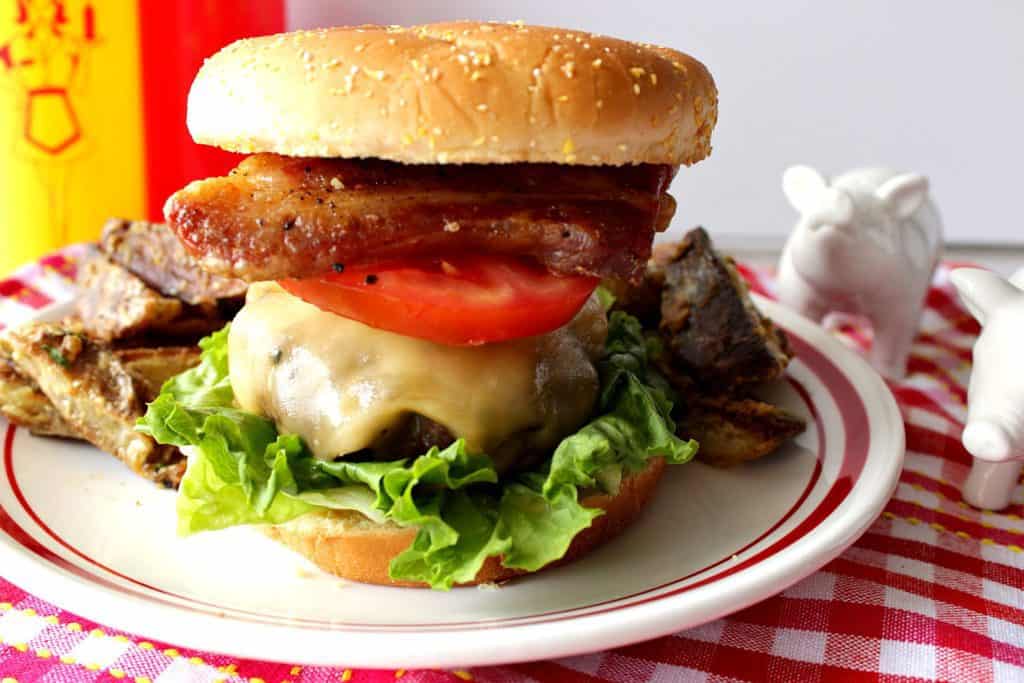 Plated Pork Belly Burger with Gouda Cheese on a red and white table cloth.