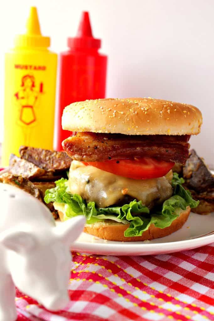 Grilled Pork Belly Burger in the foreground and a squeeze bottles of ketchup and mustard in the background.