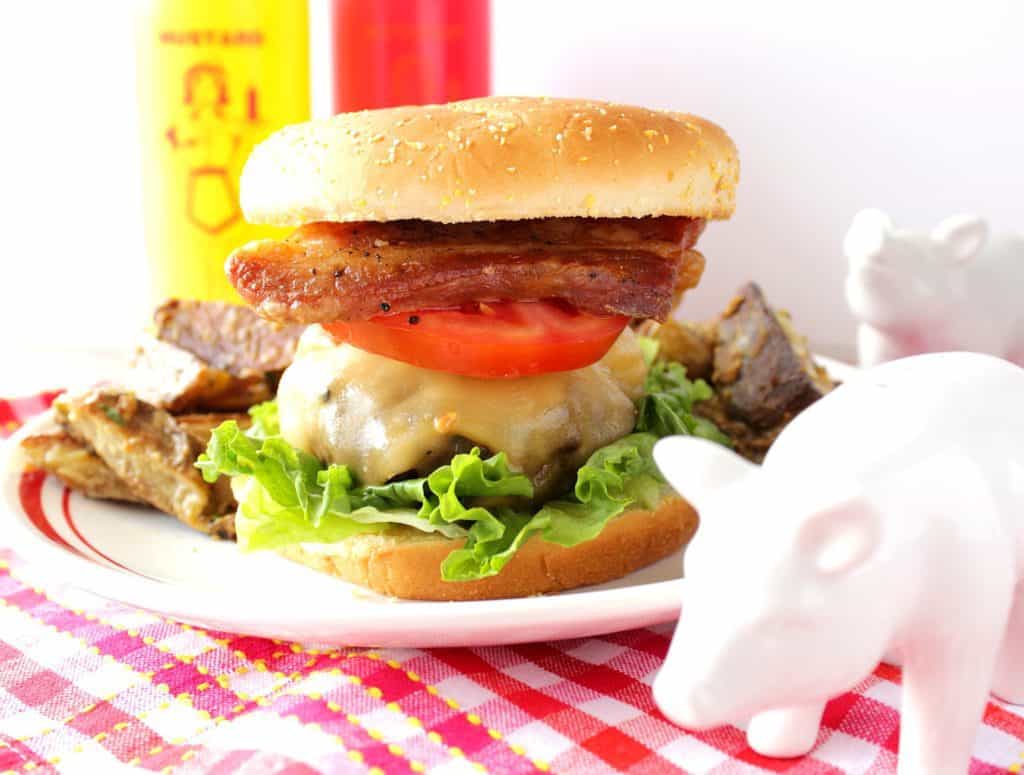 Pork Belly Burger with Gouda cheese on a plate with lettuce, tomato and pork belly slices.