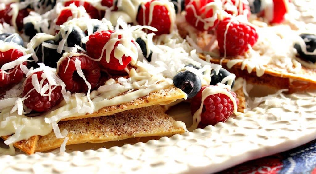 Closeup photo of a platter of crispy cinnamon sugar dessert nachos with white chocolate and berries.