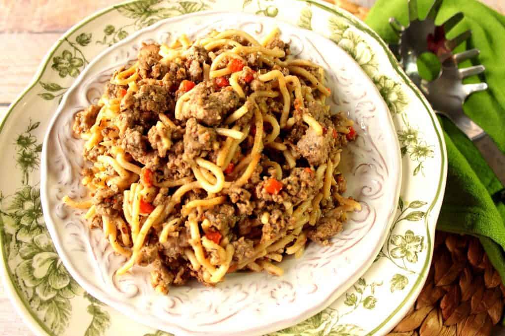 An overhead photo of Turkey Bolognese over spaghetti in a pretty white bowl with a green and white charger.