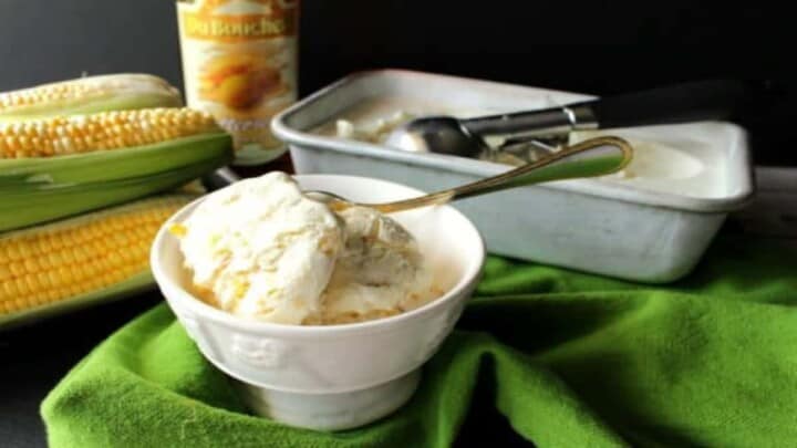 A small white bowl filled with no-churn roasted sweet corn ice cream in the foreground with ears of corn and a loaf pan filled with ice cream in the background.