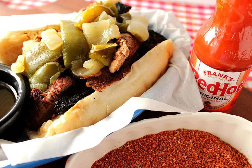 A closeup photo of a dry rub skirt steak sandwich loaded with sauteed onions and peppers with a spice blend in the foreground.