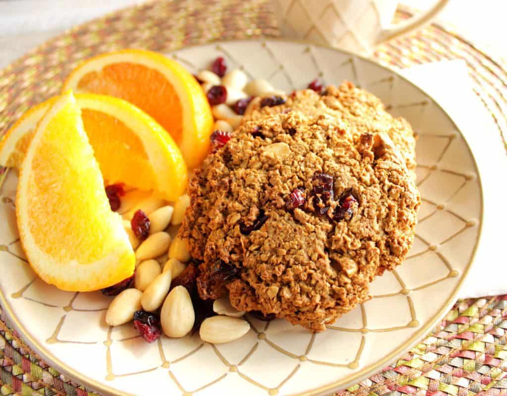 Overhead photo of gluten-free breakfast cookies on a plate with orange slices, almonds, and dried cranberries.