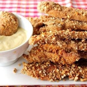 A stack of pretzel pecan coated chicken tenders with a dipping sauce.