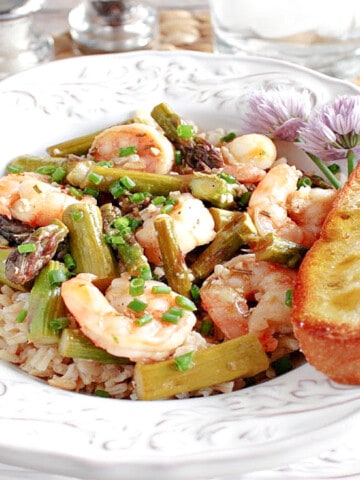 A pretty white bowl filled with Shrimp and Asparagus along with brown rice and a piece of garlic bread.