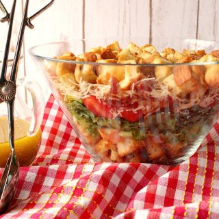 A glass bowl filled with a BLT layered salad on a red and white checked napkin.