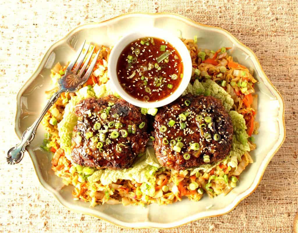 Overhead photo of two duck burgers on a plate with orange sauce, sesame seeds, and scallions.