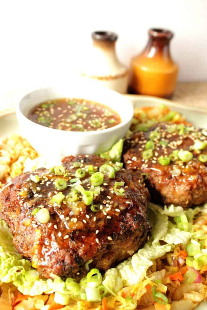 Closeup photo of a crispy duck patty on a plate with orange dipping sauce, scallions, and sesame seeds.