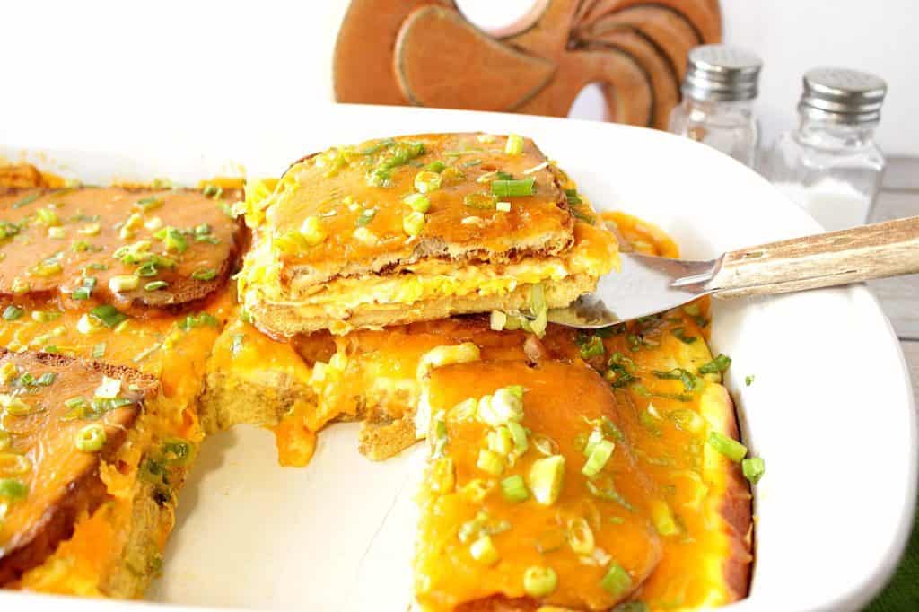 A horizontal photo of a spatula lifting a slice of egg sandwich breakfast casserole out of a dish.