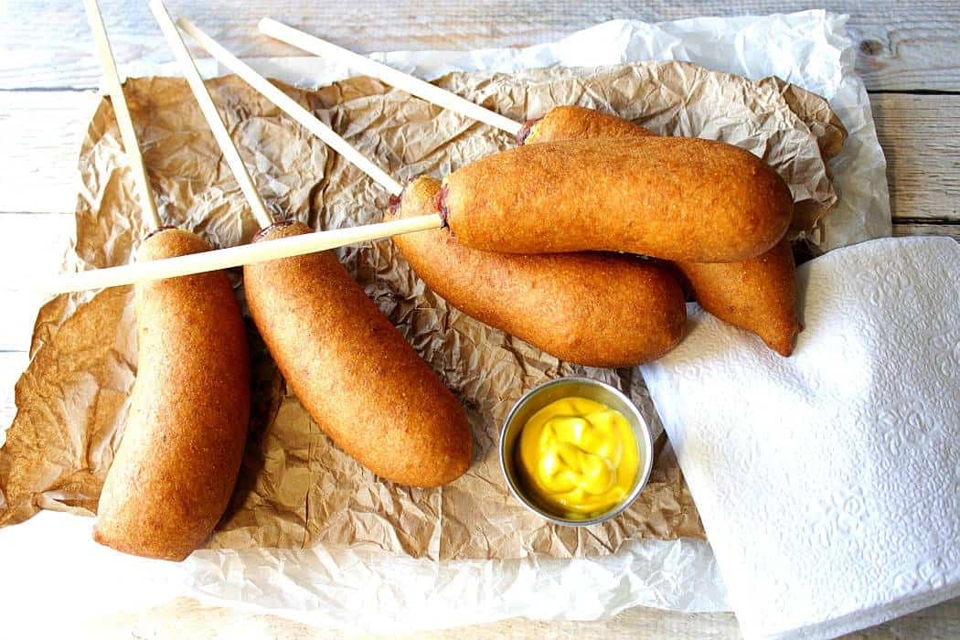 Overhead photo of beer batter bratwurst on sticks with yellow mustard and napkins