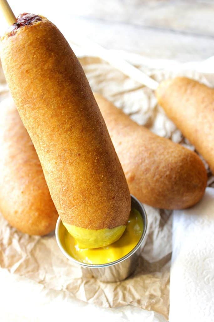 Vertical image of a beer batter bratwurst being dipped in mustard.