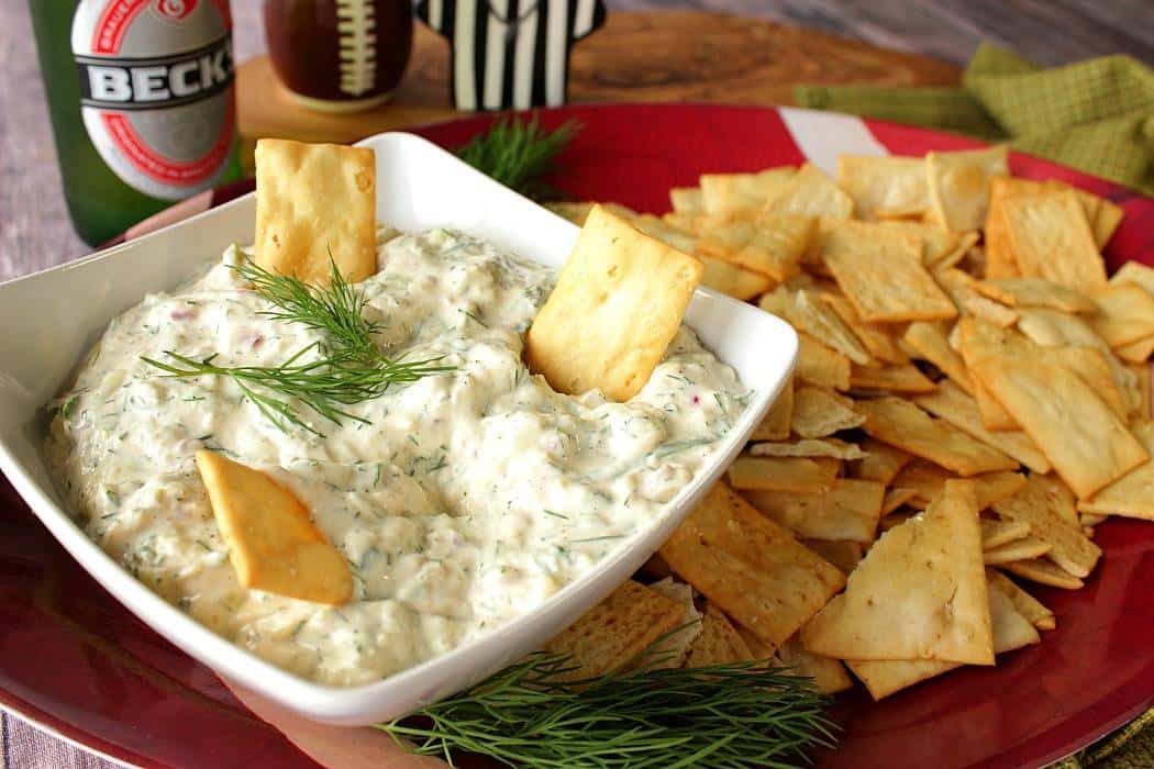 Cucumber dill dip in a bowl with crackers on the side and fresh dill sprig in the center.