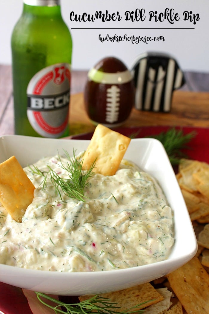 Closeup photo of cucumber dill dip with crackers and fresh dill in a square white bowl.